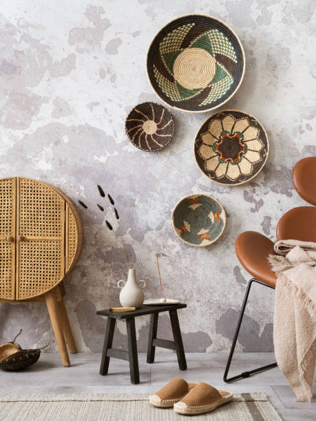 istock Creative composition of ethnic living room interior with colorful baskets, rattan sideboard, brown armchair and elegant personal accessories. Grey concrete wall. Home decor. Template. 1440015859