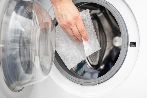 A hand dropping dryer aromatic sheets in a washing machine