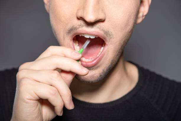 istock Man with interdental tooth brush hold handle into open mouth ready to clean space between teeth 1440016489