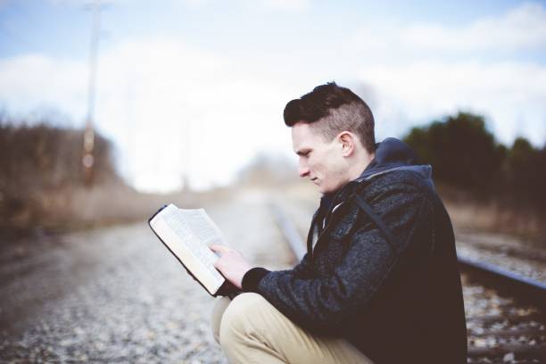 płytkie ujęcie mężczyzny siedzącego na torach kolejowych i czytającego biblię - sitting young men book isolated on white zdjęcia i obrazy z banku zdjęć