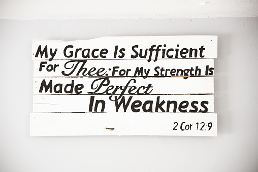 A closeup shot of a white wooden sign with a bible quote and a white background