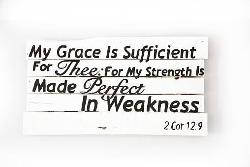 A closeup shot of a white wooden sign with bible quote written on it on a white surface