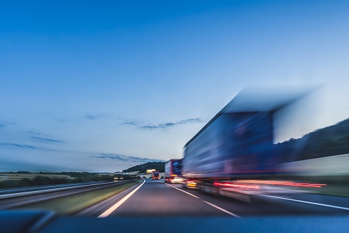 Background photograph of a highway, trucks on a highway, motion blur, light trails. Evening or night shot of trucks doing transportation