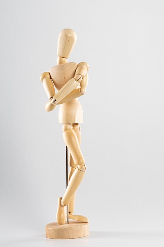 A vertical shot of a wooden pose doll with crossed arms on a white background