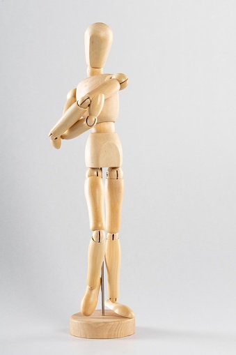 A vertical shot of a wooden pose doll stretching its arms with a white background