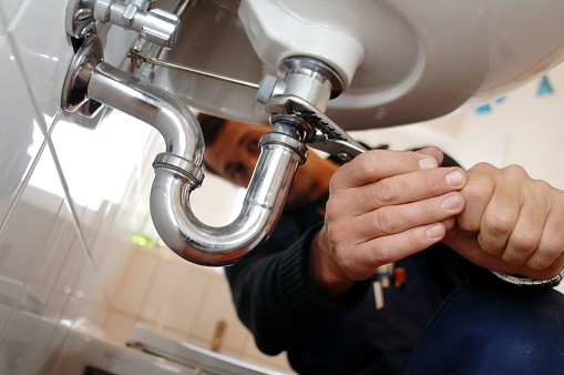 Male mechanic fixing sink. Close-up of male repairing appliance mounted on wall. He is working on equipment with metallic tools in bathroom at home.
