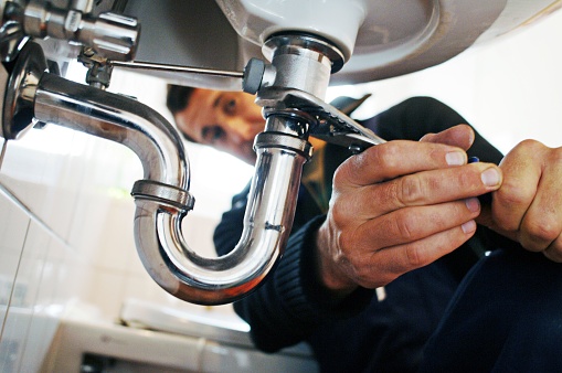 Close-up of plumber repairing sink. Male worker using tool while fixing appliance in bathroom. He is working on metallic equipment at home.