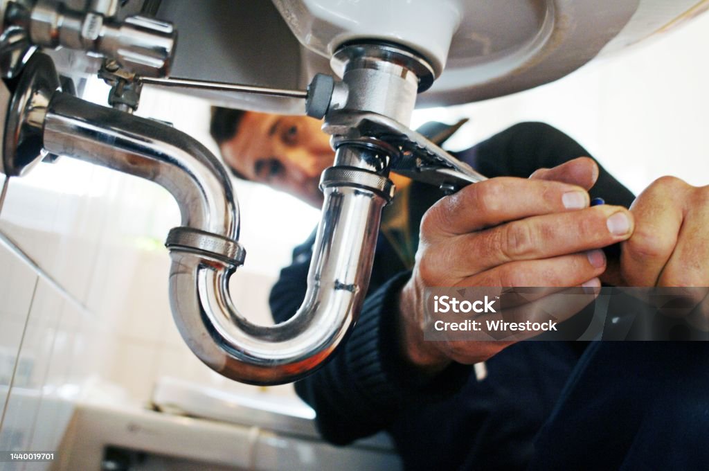 Close-up of plumber repairing sink with tool in bathroom Close-up of plumber repairing sink. Male worker using tool while fixing appliance in bathroom. He is working on metallic equipment at home. Plumber Stock Photo
