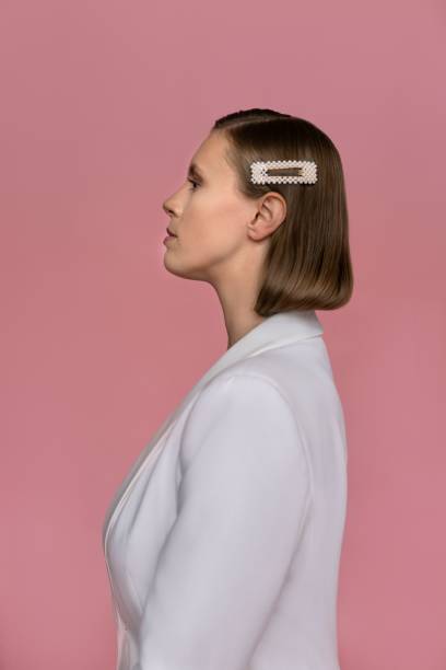 Profile view of woman in white suit standing against pink background Profile view of young woman wearing white suit. Attractive female model is standing against pink background. She is wearing head accessory in studio. hair clip stock pictures, royalty-free photos & images