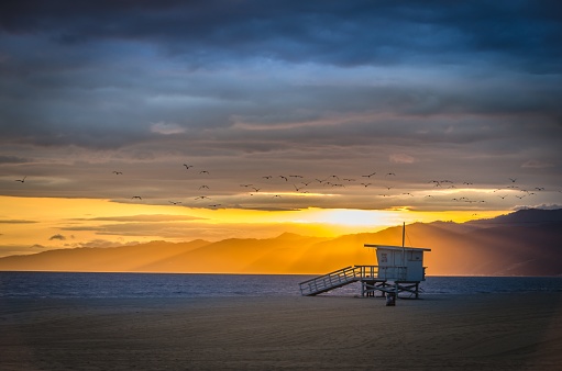 A beautiful shot of the Venice Beach with mountains in the distance under a cloudy sky at sunset