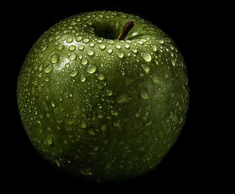 A closeup shot of a fresh green apple covered with water drops isolated on a black background