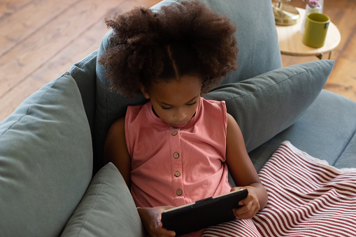 Top view of little girl reading electronic book. African American girl with curly hair, looking at electronic book or tablet. Education, leisure, technology concept
