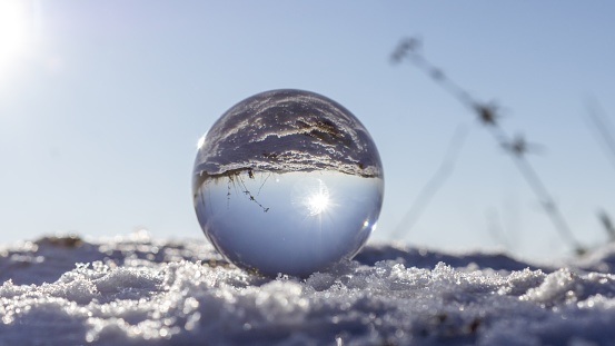 A closeup shot of a glass ball on snow reflecting the ground and the sun. Perfect for a wallpaper