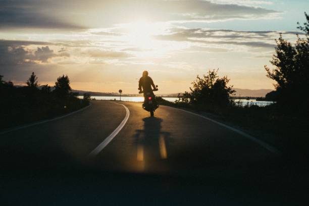 persona che guida una moto su una strada stretta durante l'ora d'oro - motorcycle biker sport city foto e immagini stock