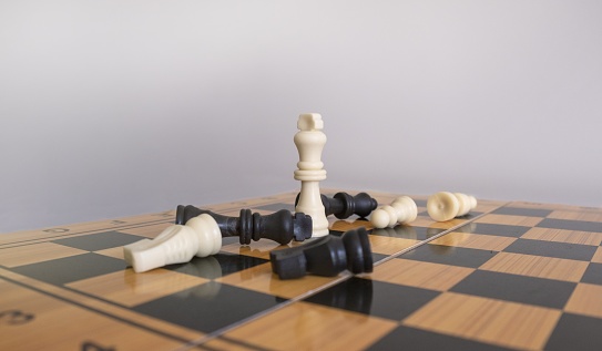 A closeup shot of chess figurines on a chessboard with a blurred white background