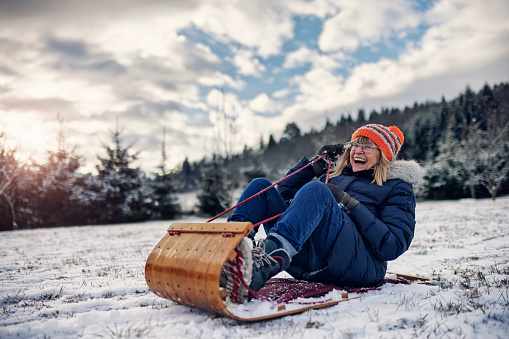 Senior woman is laughing and shouting while sledding on a winter day.
Shot with Canon R5.