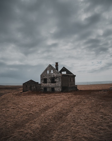 A beautiful shot of an old abandoned and half-destroyed house in a large brownfield under the gray sky - mystery/horror concept