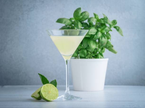 Wide shot of lime Martini in a cocktail glass near lime and mint and a basil plant in a white pot A wide shot of lime Martini in a cocktail glass near lime and mint and a basil plant in a white pot lime basil plant stock pictures, royalty-free photos & images