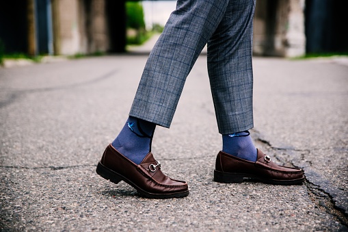 A selective closeup shot of a person wearing blue pants and brown shoes with blue socks