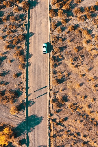 An overhead aerial drone shot of a narrow desert road with a car on the side of the road