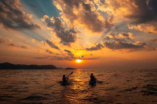 A female and a male sailing with canoes close to each other at sunset
