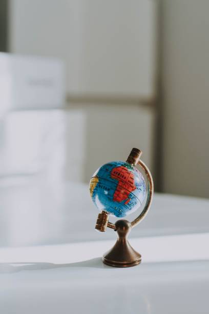 istock Vertical closeup shot of a decorative small globe on a white desk and blurred background 1440026360