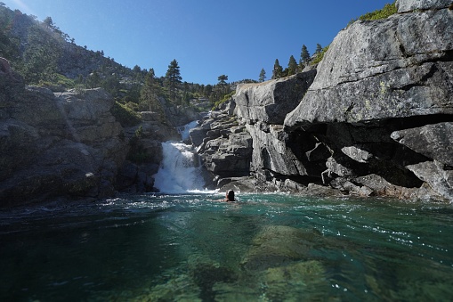 A waterfall flowing down from rocky cliffs to a pond with female swimming on a sunny day at Horsetail Falls near Lake Tahoe, CA