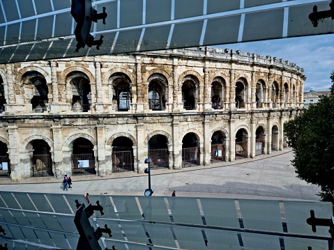 The Musée de la Romanité is a museum with a huge collection of artefacts from the roman empire found arround Nimes.  It opened for the public on June 2, 2018. The architect was Elizabeth de Portzamparc. The image shows a feature of the facade and the Arena of Nîmes, captured during autumn season.
