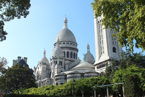 A low angle shot of the famous Basilica of the Sacred Heart of Paris, France with clear blue sky in the background and greenery around