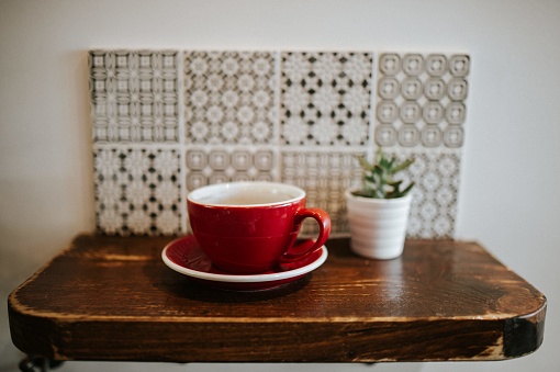A closeup shot of a red ceramic cup and a flower pot on a small wooden surface