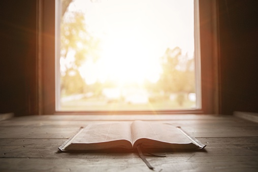A close shot of holy bible on a wooden surface with the sun shining in the background