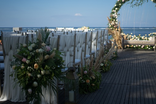 A shot of decorated arch and white chairs for a wedding ceremony near the body of water