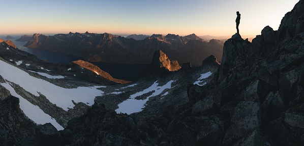 A wide shot of a male standing on a rock on a high rocky mountain enjoying the beautiful view during sunrise