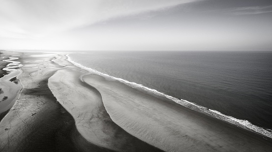 An aerial greyscale shot of a sandy beach near the peaceful ocean