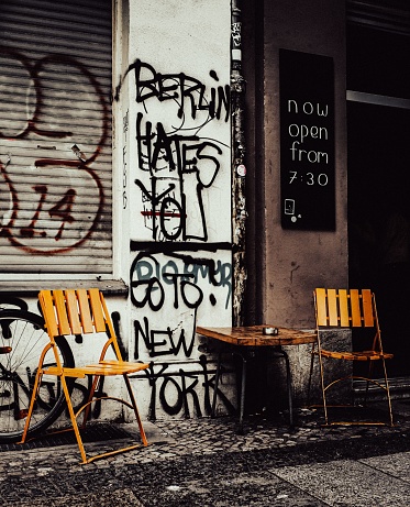 Berlin, Germany – September 21, 2019: The vertical view of empty wooden chairs and a table placed before the graffiti wall in Kreuzberg