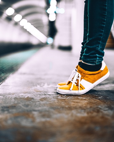 A vertical selective closeup shot of a person wearing yellow and white sneakers and blue tight pants
