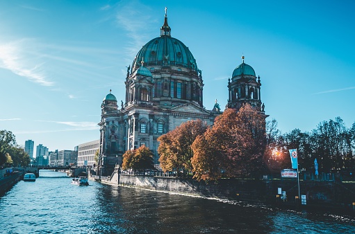 Wide shot of trees with orange leaves near Berlin Cathedral by the water under a blue sky