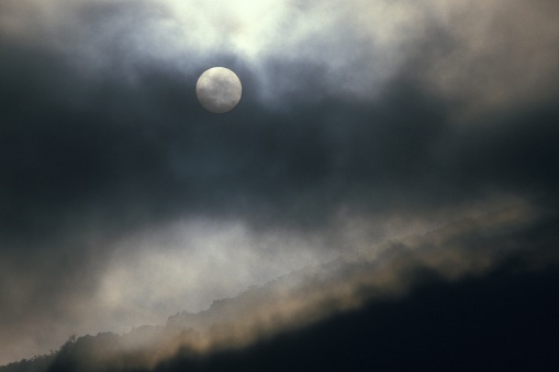 A wide shot of a full moon covered with dark gray clouds in the sky