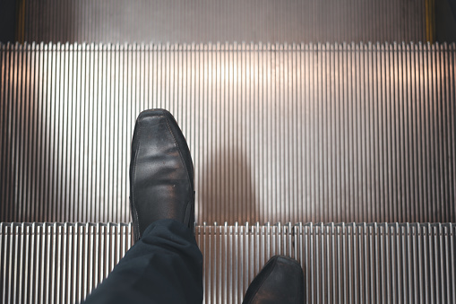 Man with pair of leather shoes down escalator. Going down