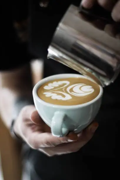 A vertical selective closeup shot of a person holding white ceramic cup with coffee with latte art