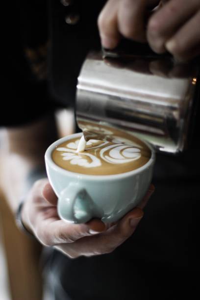 istock a person pouring milk in a white ceramic cup with coffee with latte art 1440035754
