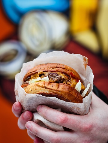 A vertical selective closeup shot of a person holding a wrapped burger