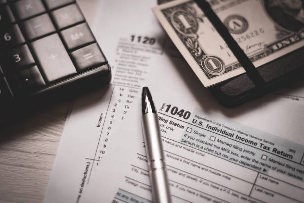 U.S. individual and corporation income tax return close-up next to a calculator, dollars, money, a pen and a notepad on a wooden table. Retro old style photo. stock photo