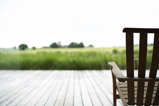 A beautiful view of a wooden chair on a porch in front of a grass covered field