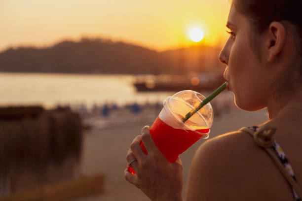 Young woman in foreground enjoying a slushy at sunset while drinking through a straw.