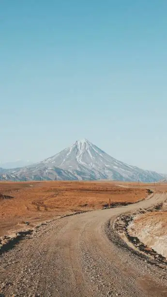 Photo of Beautiful vertical shot of a narrow curvy and muddy road with a high mountain in the background