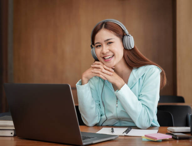istock Female student in headphone is using laptop to studying online learning and taking notes in notebook 1440038613