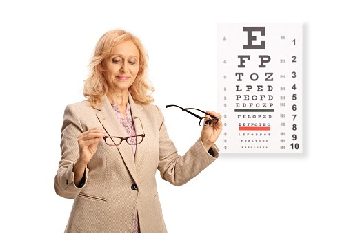 Woman comparing two pairs of eyesight glasses in front of a vision test isolated on white background