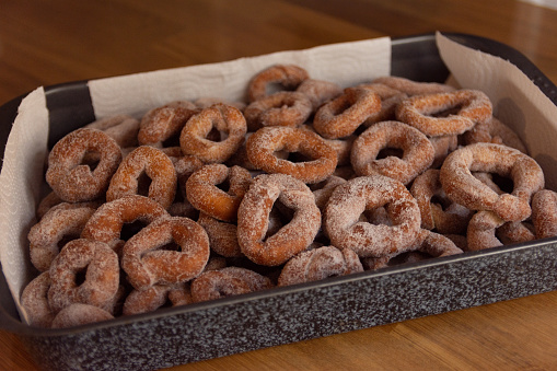 freshly finished spanish christmas icing sugar donuts in a black-gray metal tray on top of a wooden surface - oblique view