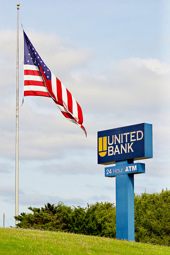 Morgantown, West Virginia, USA - May 5, 2022: An American flag waves in the breeze next to a “United Bank” sign on the side of a highway.